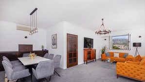 Un salon moderne avec un coin repas, une grande fenêtre donnant sur la ville et un confortable canapé orange.