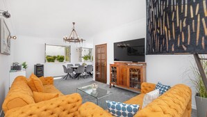 Un salon moderne comprenant un grand ensemble de canapés, une table basse en verre et un coin repas avec des chaises et un lustre.