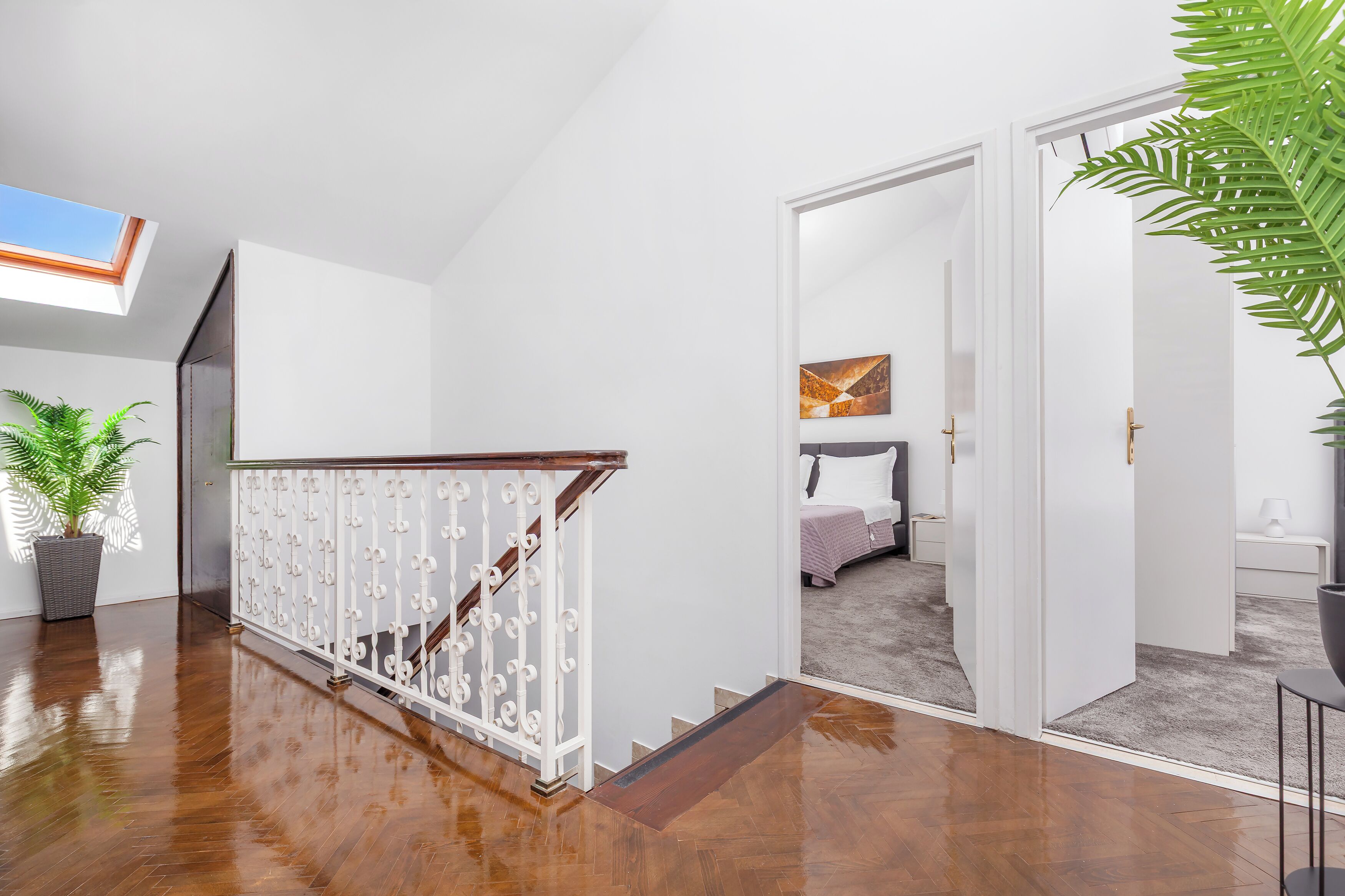 Un intérieur moderne avec un escalier en bois, une plante en pot et une vue sur une chambre à coucher, visible à travers une porte ouverte.
