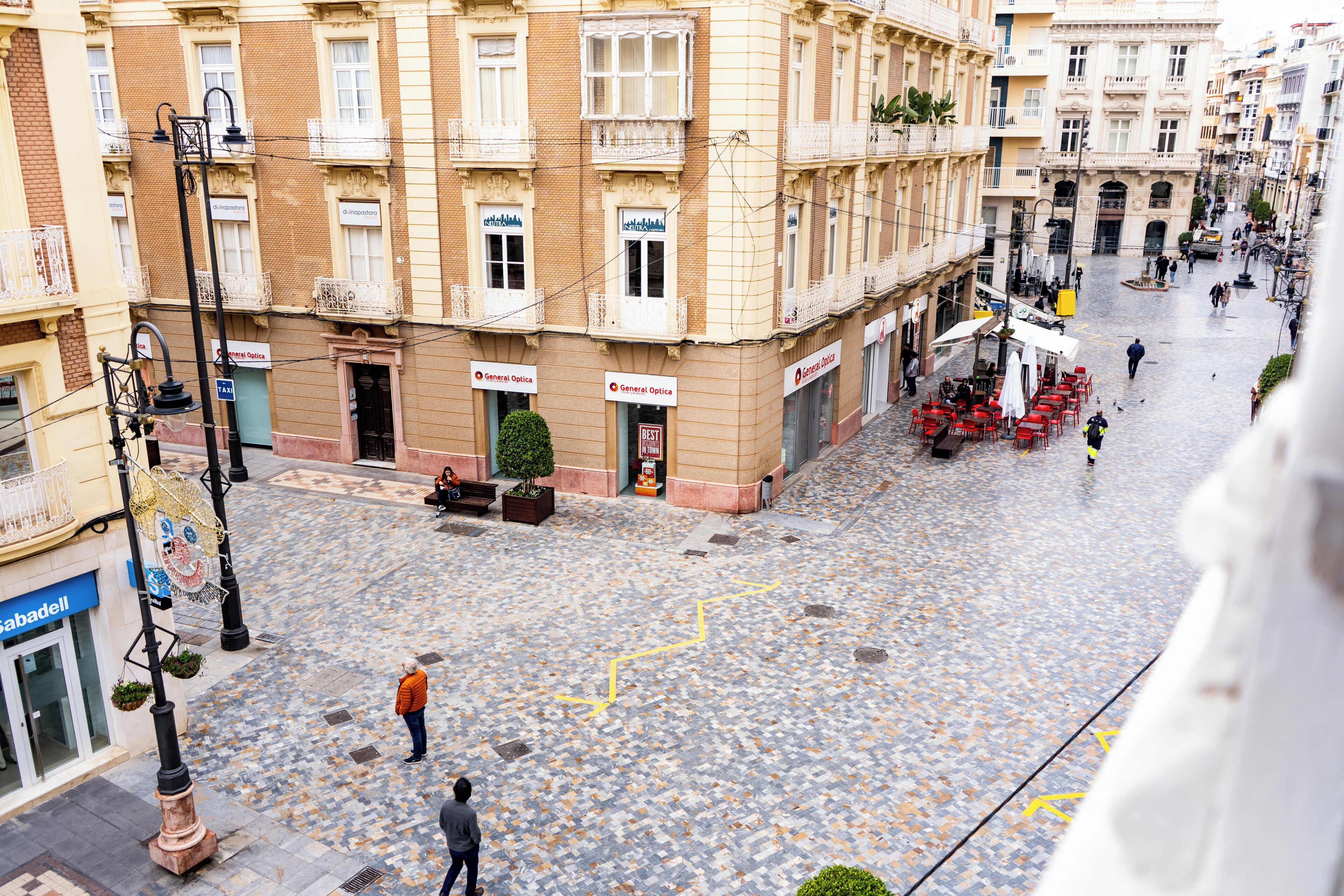 A cobblestone square with buildings, outdoor seating, and a few pedestrians.