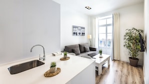 A modern kitchen with a white countertop, stainless steel sink, and a grey sofa in the living area.