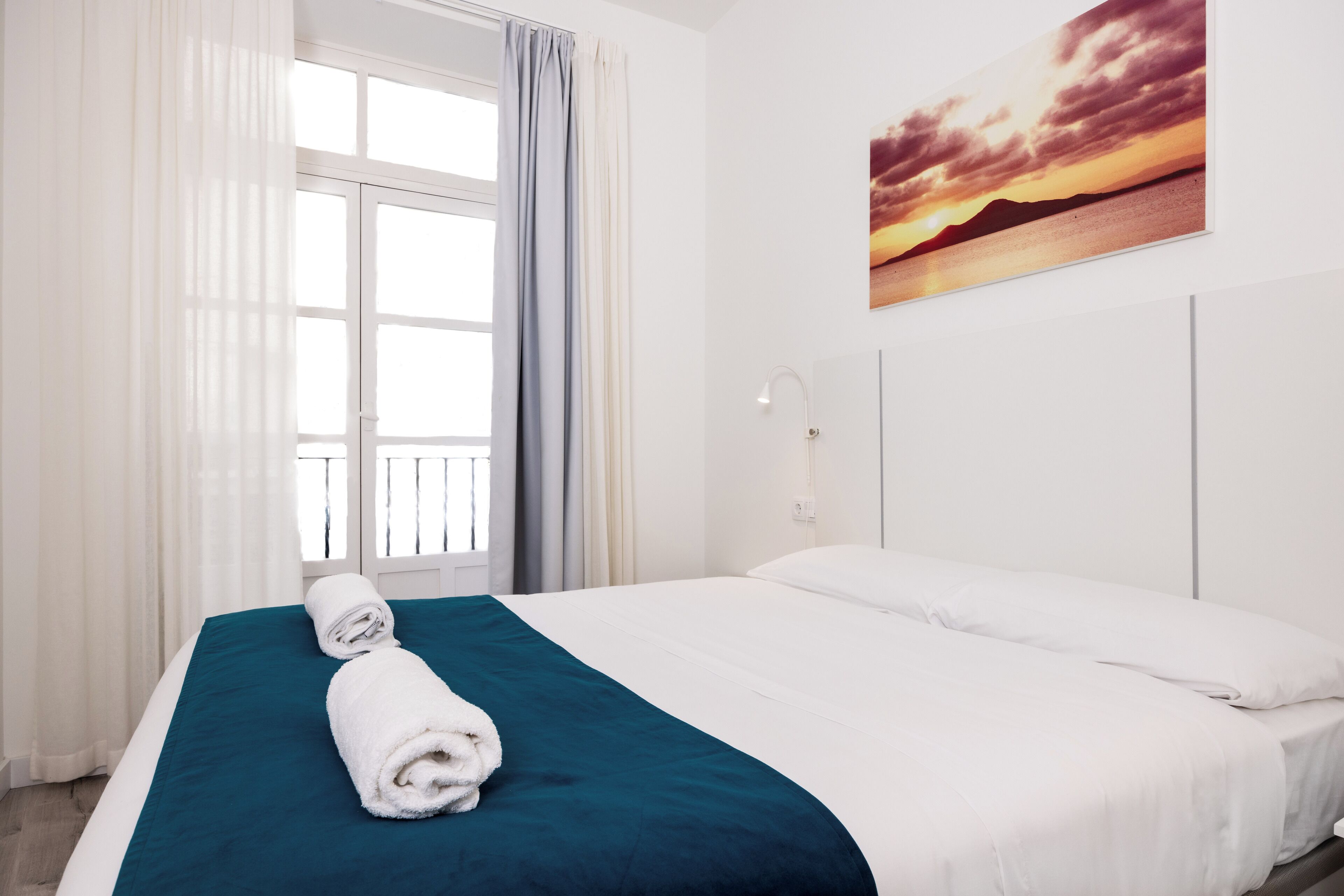 A hotel room with a bed, a window with curtains, and a painting on the wall.