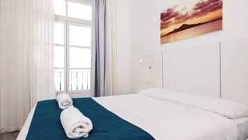 A hotel room with a bed, a window with curtains, and a painting on the wall.