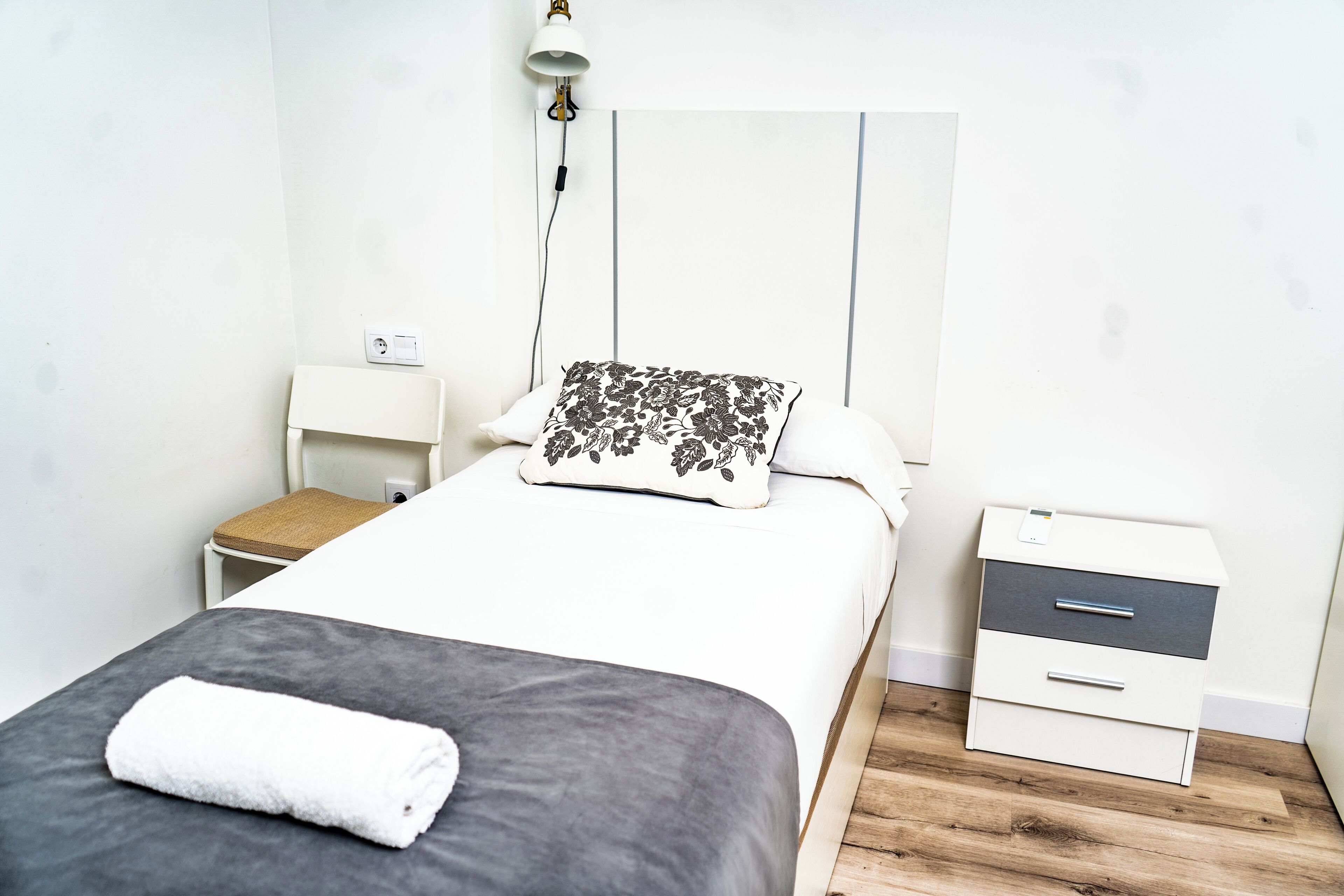 A neatly arranged bedroom with a bed, a bedside table, a chair, and a nightstand.