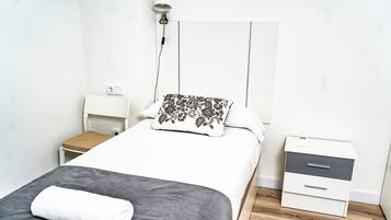 Un dormitorio ordenado con cama, mesita de noche, silla y tocador.
