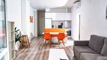 Una sala de estar moderna con un sofá gris, una mesa de centro blanca y dos sillas naranjas.