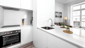 A modern kitchen with white cabinetry, a built-in oven, a stainless steel sink, and a dining area with a white countertop.