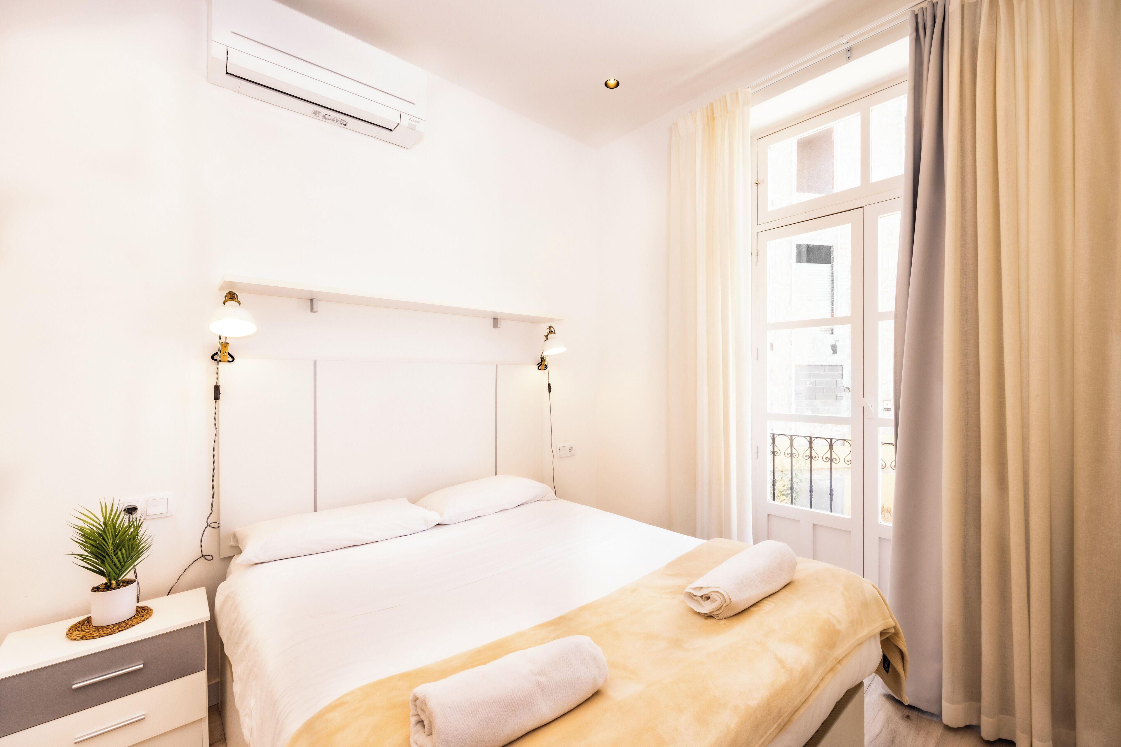 Habitación de hotel con cama, mesita de noche, lámpara y ventana con cortinas.