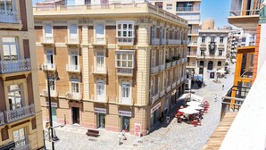 A building with multiple balconies, a cobblestone street, and outdoor seating areas.
