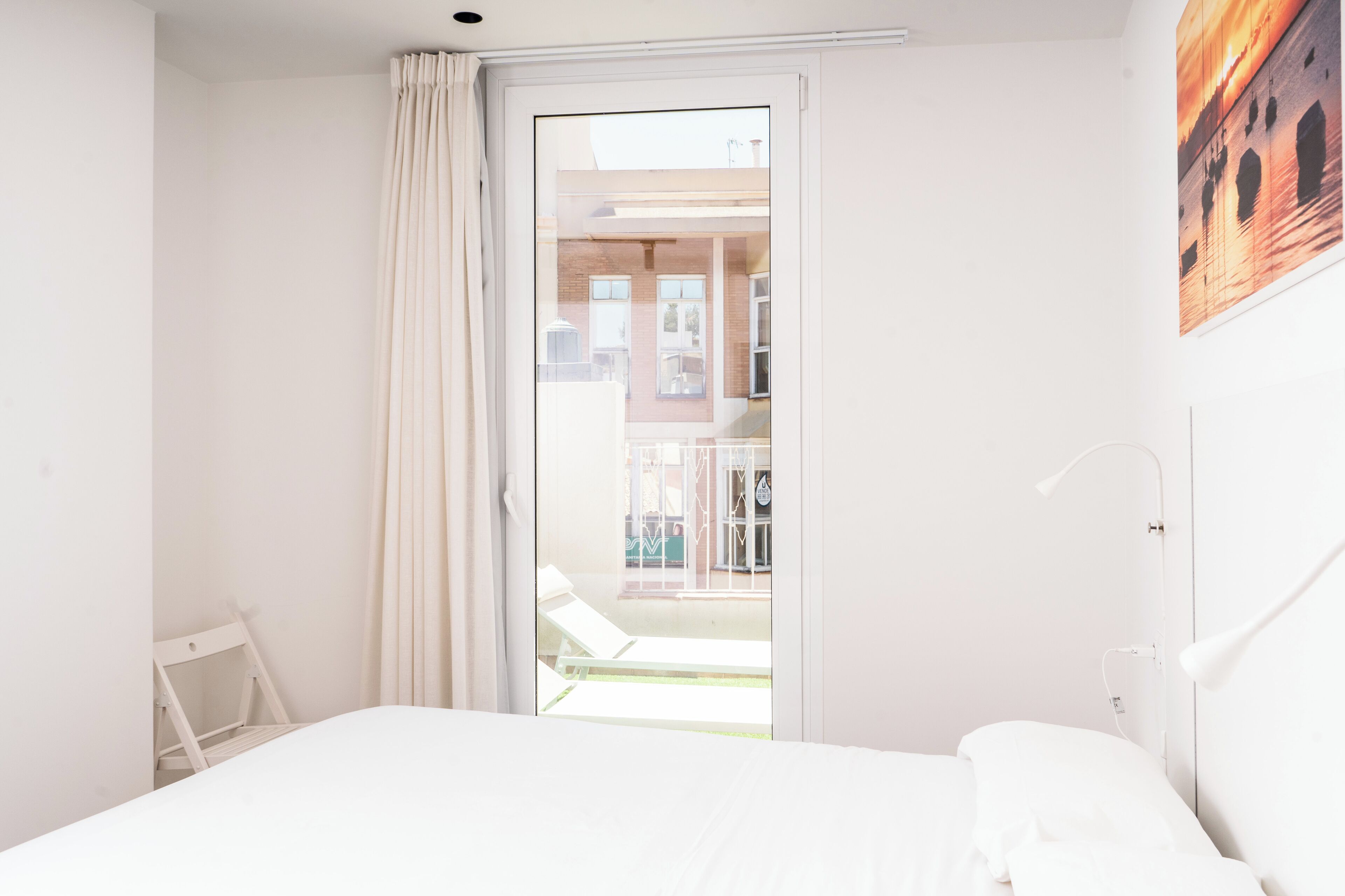 Un dormitorio con cama, mesita de noche, lámpara y vistas al balcón exterior.