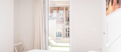 Un dormitorio con cama, mesita de noche, lámpara y vistas al balcón exterior.