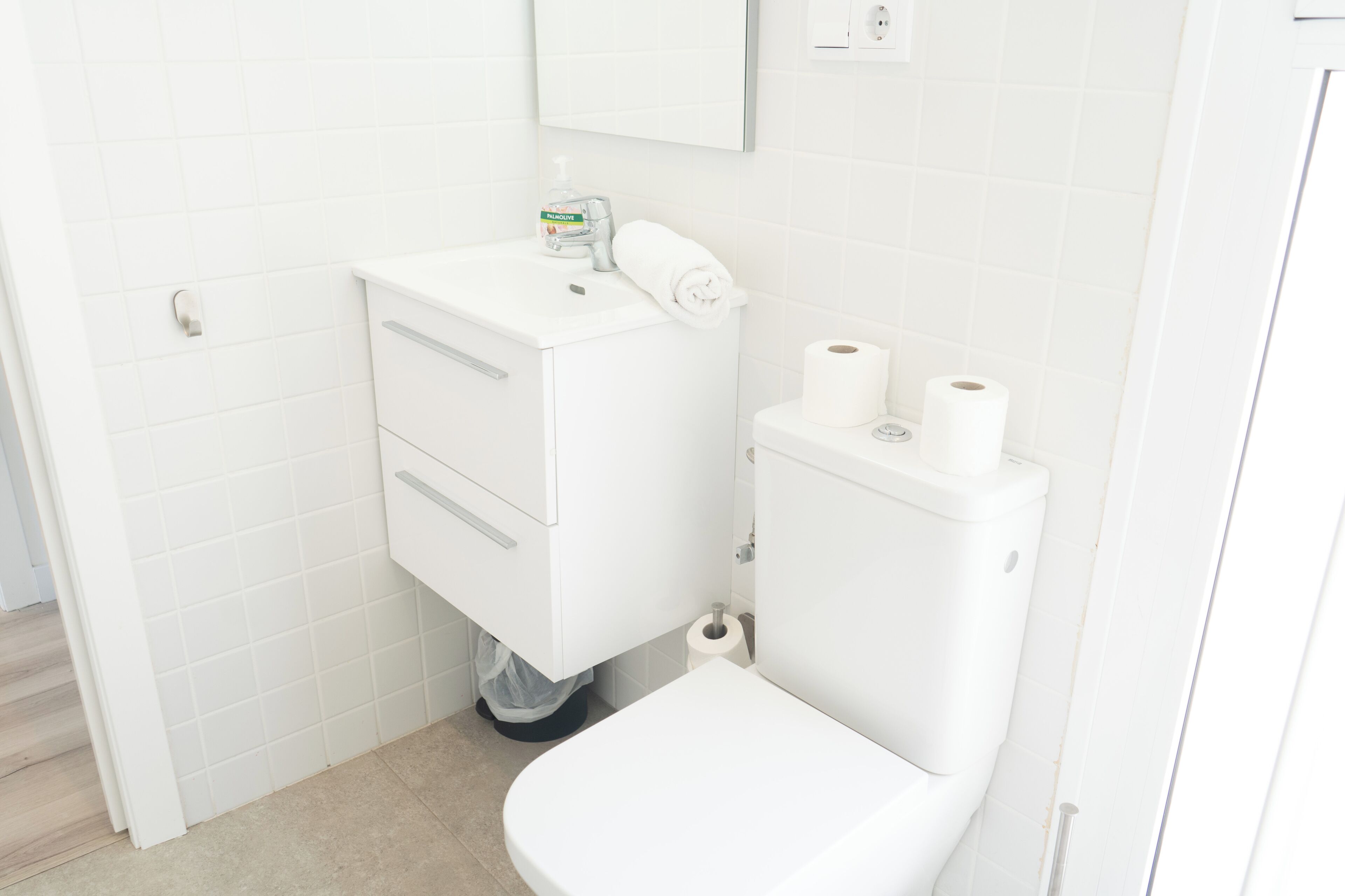 Un baño pequeño y limpio con lavamanos blanco, inodoro y espejo sobre el lavamanos.