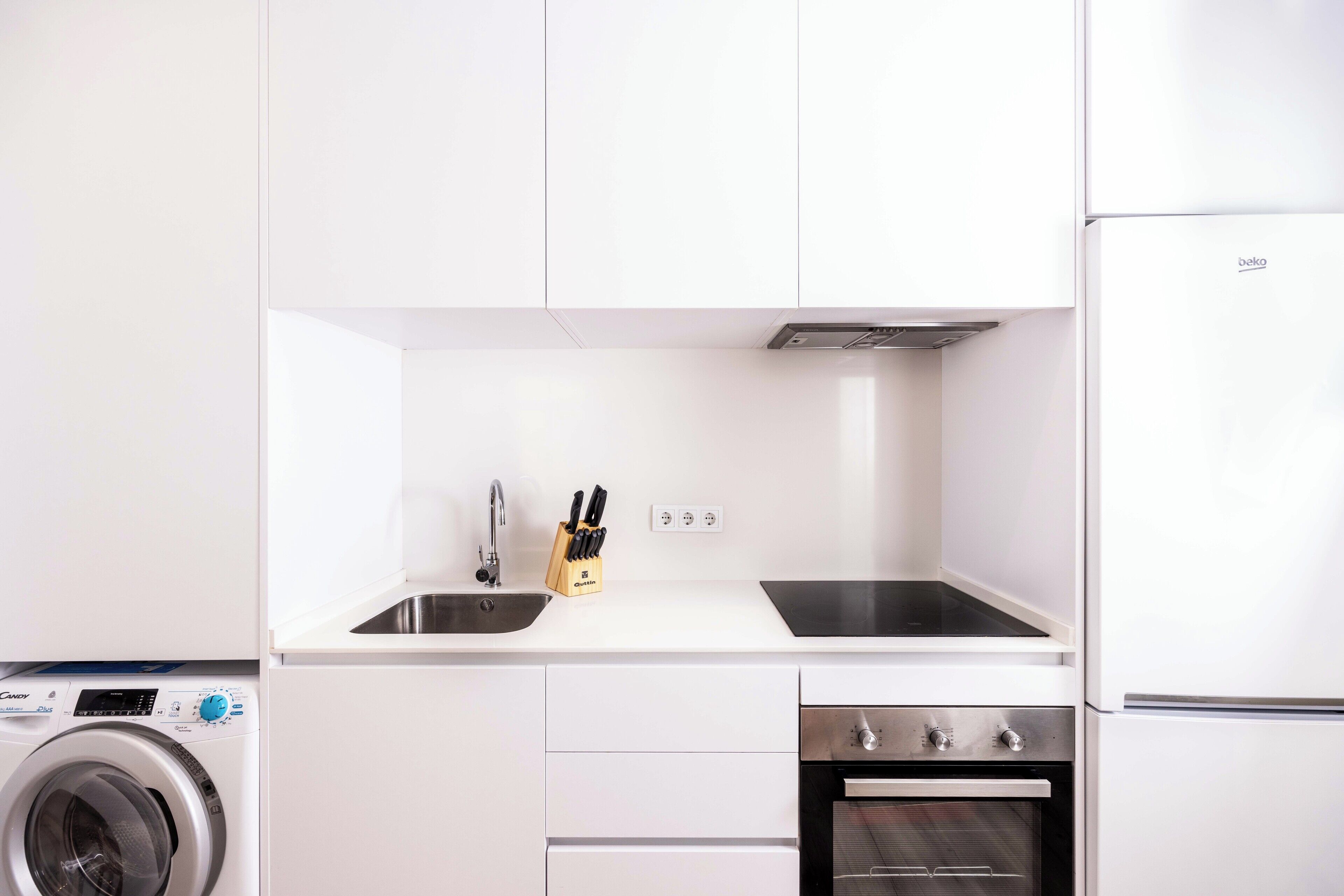 A modern kitchen with white cabinets, a built-in washing machine, a sink, and a stove.