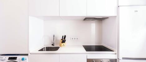 A modern kitchen with white cabinets, a built-in washing machine, a sink, and a stove.