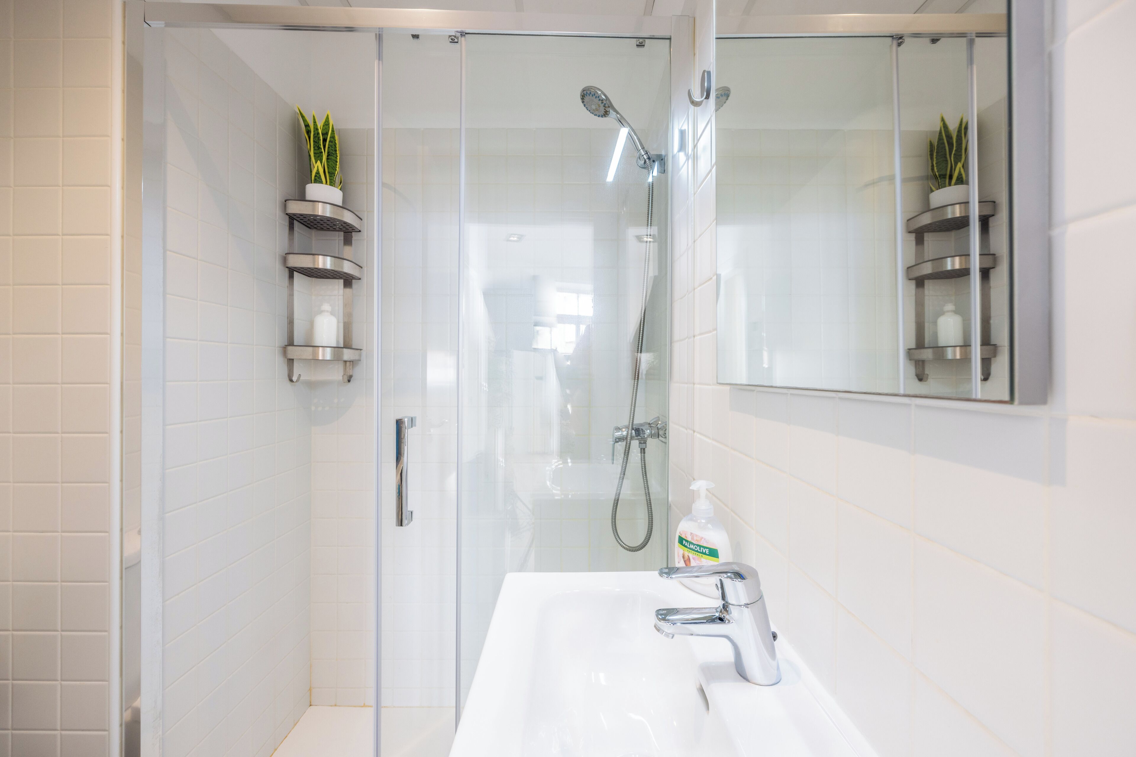 A modern bathroom with a glass-enclosed shower, a white sink with a chrome faucet, and a mirrored wall above the sink.