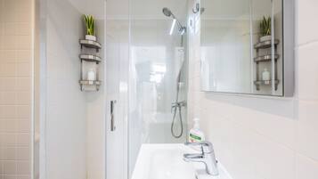 Un bany modern amb dutxa de vidre, un lavabo blanc amb aixeta cromada i un mirall sobre el lavabo.