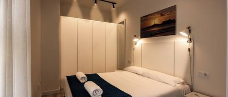A hotel room with a bed, a nightstand, a wall-mounted lamp, and a painting.