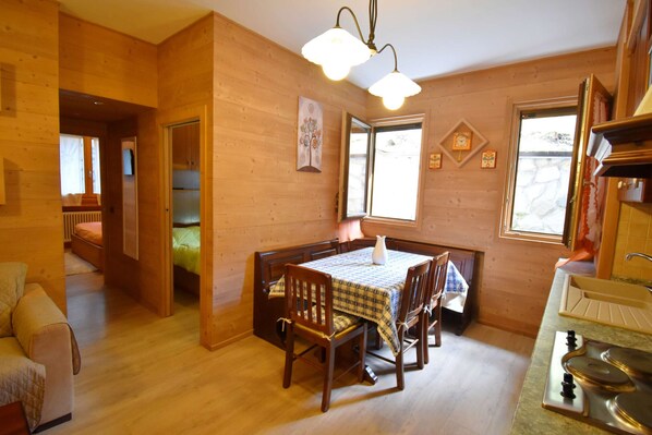 A wooden interior with a dining table, chairs, a kitchen area, and a cozy seating area. - Nambino On The Slopes (Madonna di Campiglio)