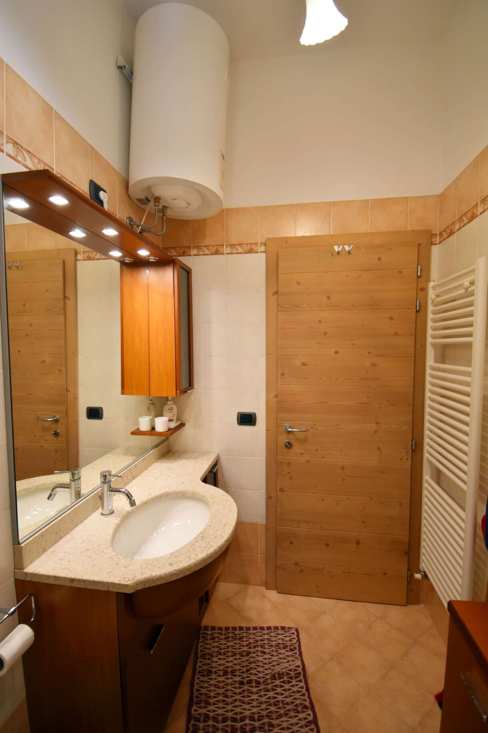Baño con lavamanos, espejo, puerta de madera y toallero.
