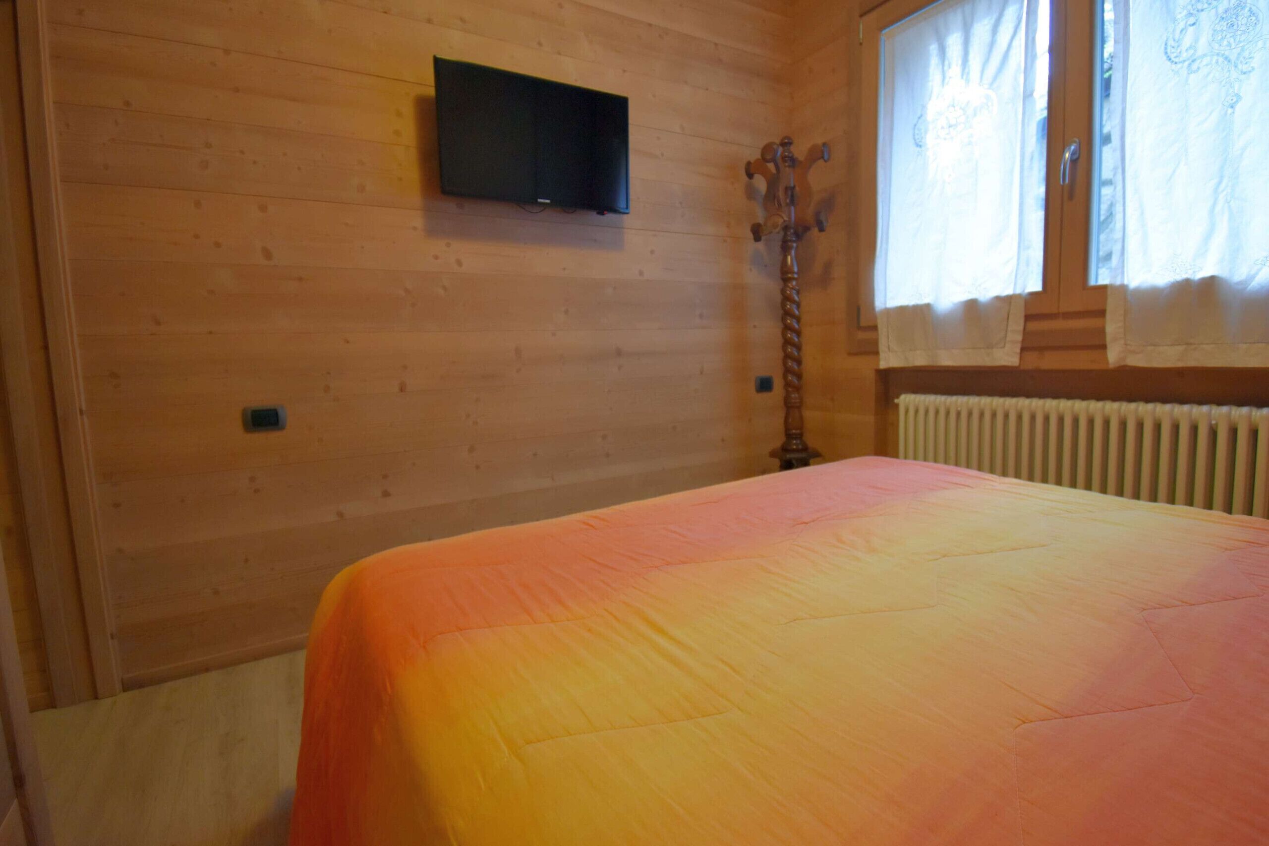 A wooden room with a bed, a television mounted on the wall, and a window with curtains.