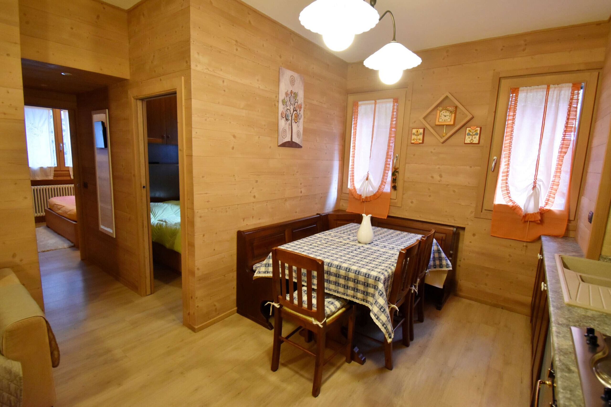 Interior em madeira com mesa de jantar, cadeiras, um vaso branco e uma área de cozinha.