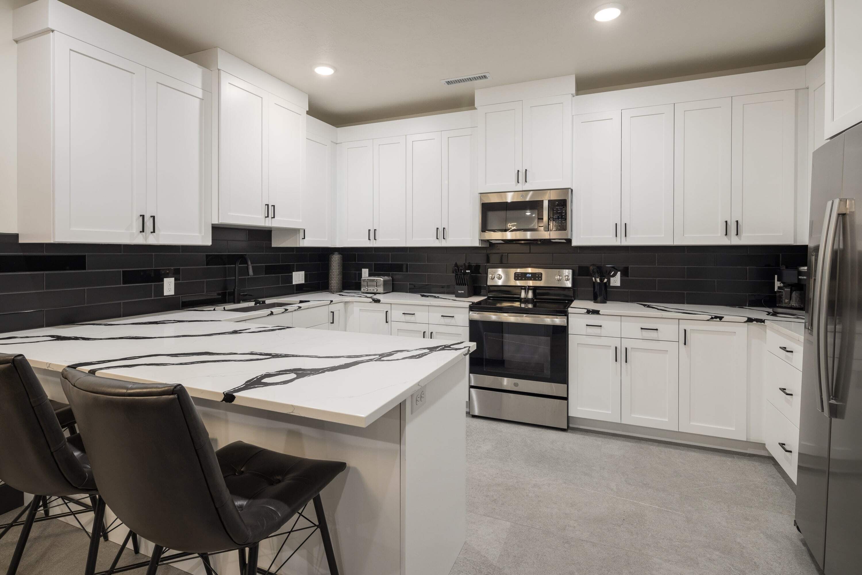 A modern kitchen with white cabinets, a central island, and stainless steel appliances. - Vizcaya #7 - Moab's Newest Luxury Rental (Moab)