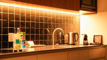 A kitchen with a tiled backsplash, a stainless steel kettle, a coffee maker, and a microwave above the counter.