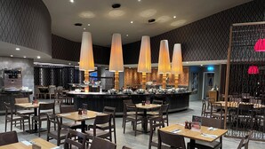 A modern restaurant with a central bar, multiple dining tables, and pendant lighting. - Peppers Gladstone (Barney Point)
