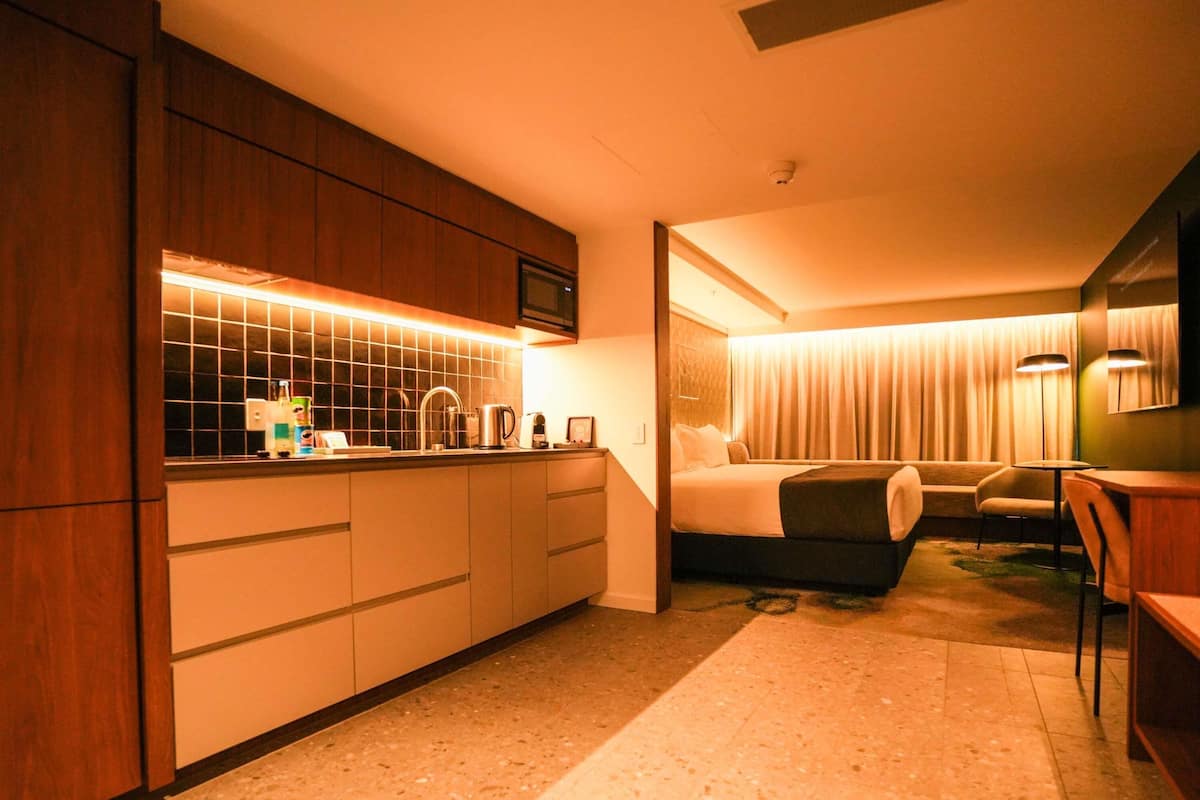 A hotel room with a kitchenette, a bed, a seating area, and a bathroom.