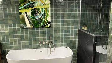 A bathroom with a freestanding bathtub, a glass shower enclosure, and a green-tiled wall.