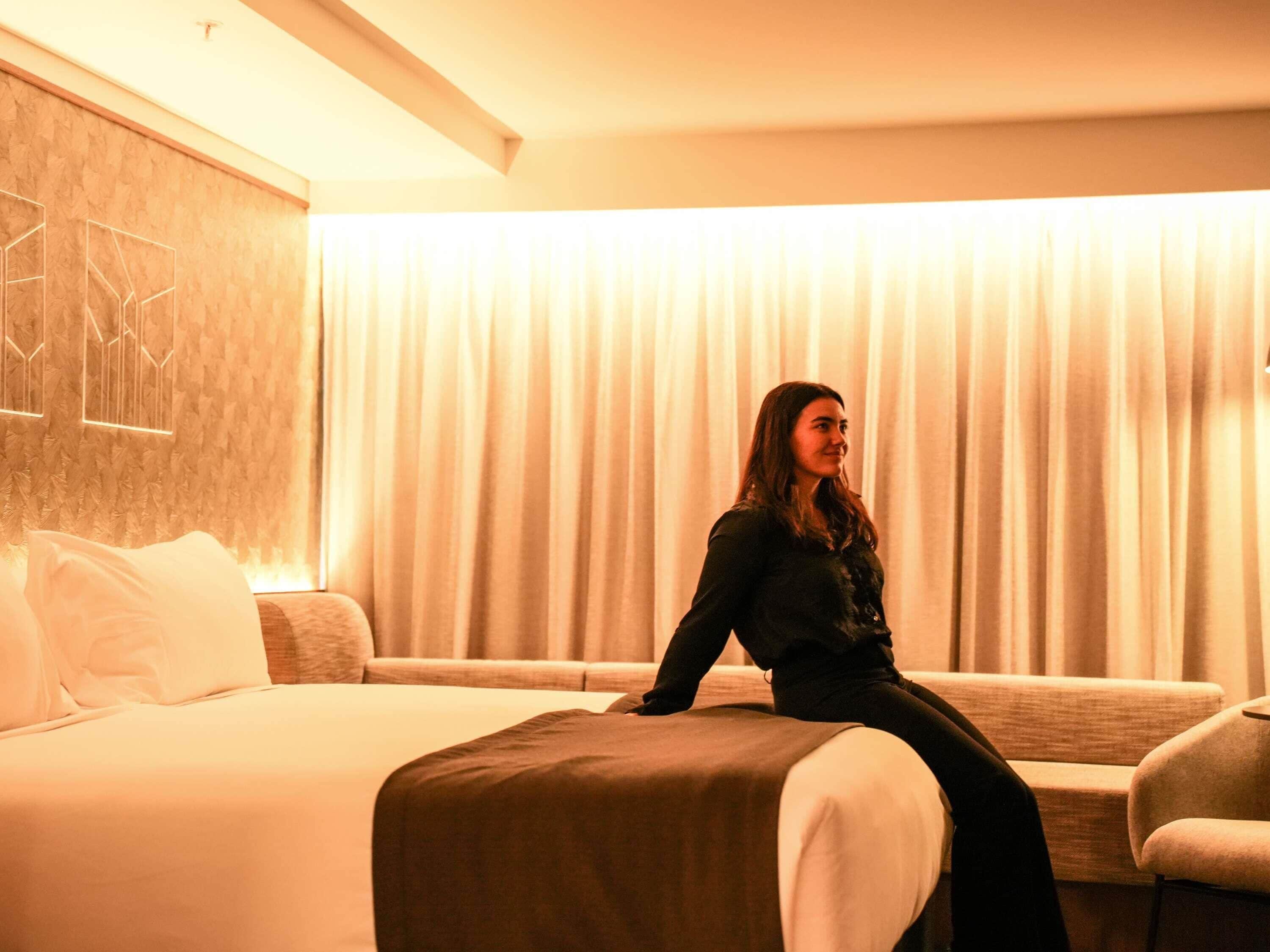 A hotel room with a bed, a sofa, and a large window with curtains.