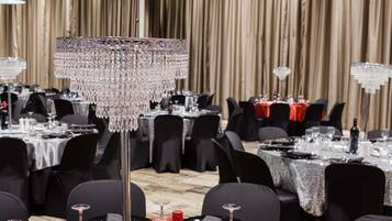 Un salón de banquetes con mesas dispuestas para comer, una araña de cristal y un mantel rojo.