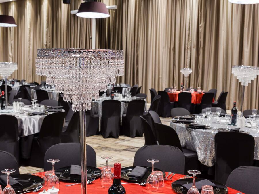Un salón de banquetes con mesas dispuestas para comer, una araña de cristal y un mantel rojo.