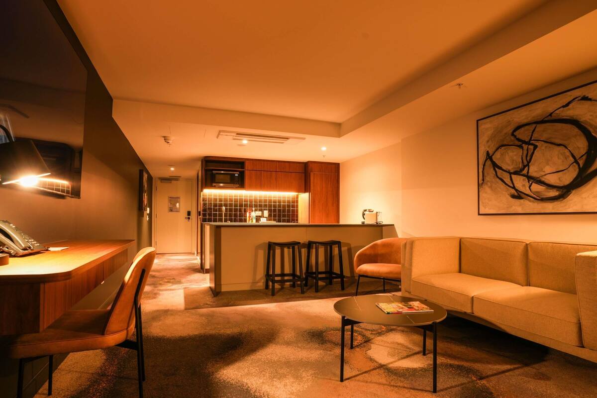 A modern living room with a sofa, a coffee table, and a kitchen area with a microwave and stools.