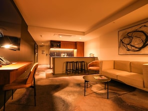 A modern living room with a sofa, a coffee table, and a kitchen area with a microwave and stools. - Peppers Gladstone (Barney Point)