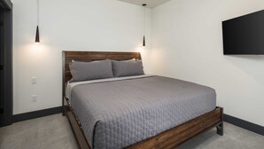 Ein Schlafzimmer mit Bett, Deckenventilator, Pendelleuchten und einem Flachbildfernseher an der Wand.