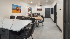 A modern dining area with a white table, black chairs, and a wooden bench. There are ceiling fans and wall-mounted lights. - Vizcaya #9 - Moab's Newest Luxury Rental (Moab)