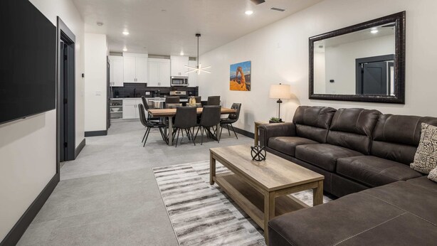 A modern living room with a brown leather sofa, a wooden coffee table, and a dining area with a black and white rug. - Vizcaya #9 - Moab's Newest Luxury Rental (Moab)