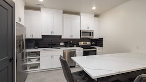 A modern kitchen with white cabinets, stainless steel appliances, and a white dining table. - Vizcaya #9 - Moab's Newest Luxury Rental (Moab)