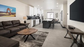 A modern living room with a sofa, coffee table, and a dining area with a kitchen in the background. - Vizcaya #12 - Moab's Newest Luxury Rental (Moab)