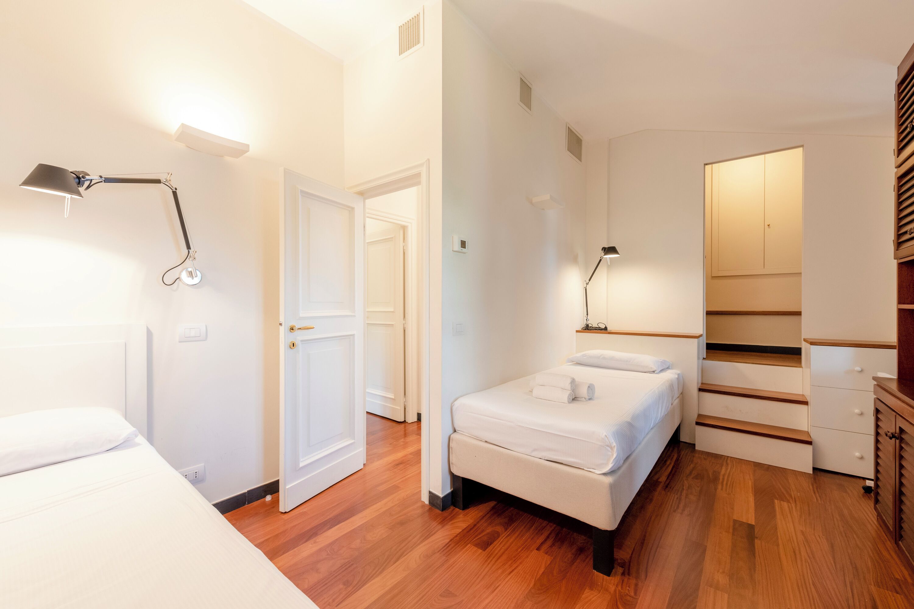 Una habitación de hotel moderna con suelo de madera, cama, escritorio y armario.