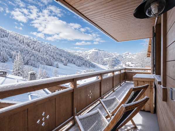 A wooden balcony with a view of snow-covered mountains and a clear sky.