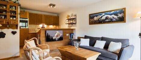 A living room with a grey sofa, wooden coffee table, wicker chairs, and a television on the wall.