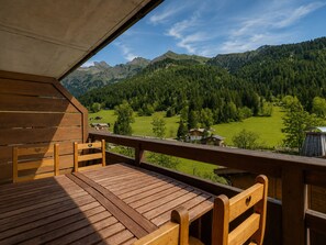 A wooden deck with a table and chairs, overlooking a mountainous landscape with houses and greenery.