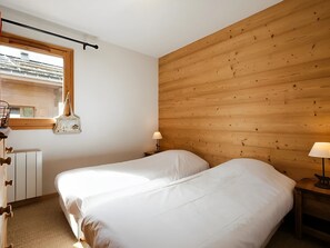 A bedroom with two beds, wooden panel walls, a window, a radiator, and a lamp on a bedside table. - 3* Apartment with Wifi - 3 Bedrooms for 6 Guests in La Clusaz (La Clusaz)