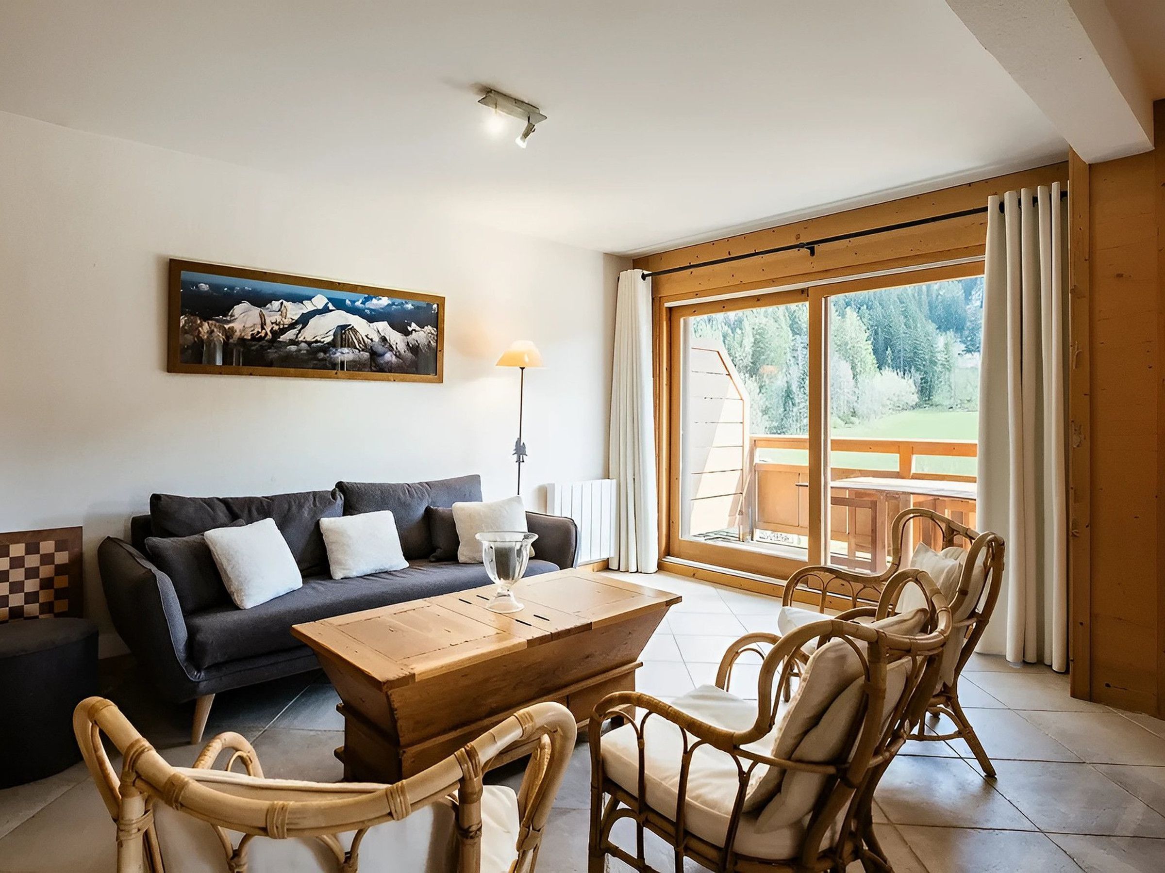 Un salon comprenant un canapé, une table basse en bois, des fauteuils en osier, un tableau et une grande fenêtre donnant sur un paysage verdoyant.