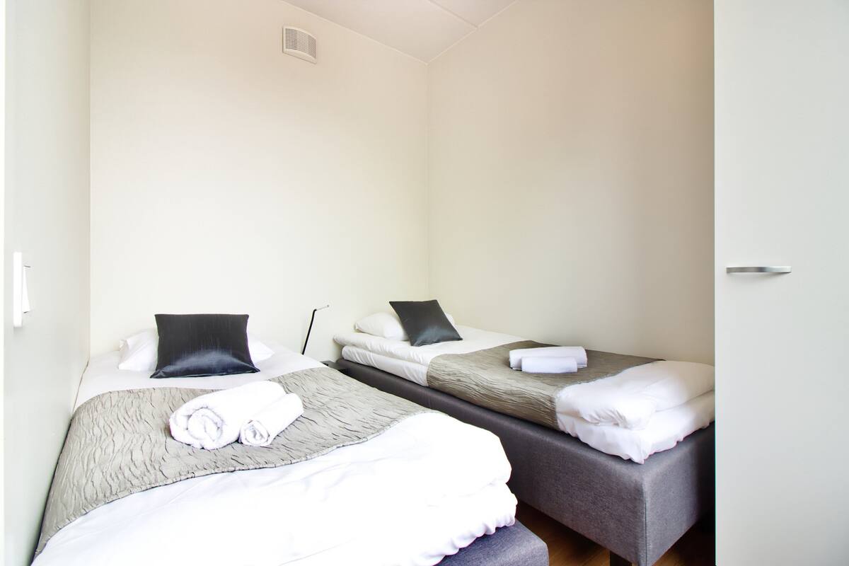 A hotel room with two single beds, each with a pillow and a rolled towel.