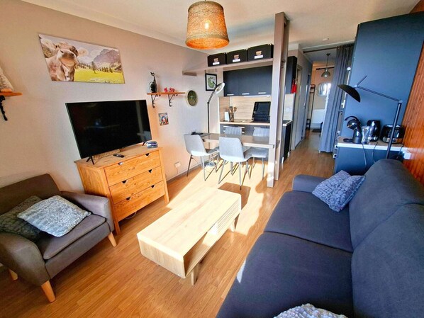 Een moderne woonkamer met een bank, televisie, houten kast en een eethoek met stoelen en een tafel.