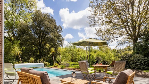 A wooden deck with outdoor furniture, a pool, and lush greenery. - Charming Stone Cottage with Heated Pool, Private Garden, and Close to Beaches (Saint-Lyphard)