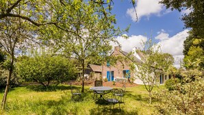 A rustic house with a thatched roof and blue shutters, surrounded by lush greenery and a grassy lawn. - Charming Stone Cottage with Heated Pool, Private Garden, and Close to Beaches (Saint-Lyphard)